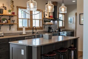 Une cuisine dotée d’un îlot central, de tabourets de bar, de luminaires suspendus et d’une fenêtre laissant entrer la lumière naturelle.