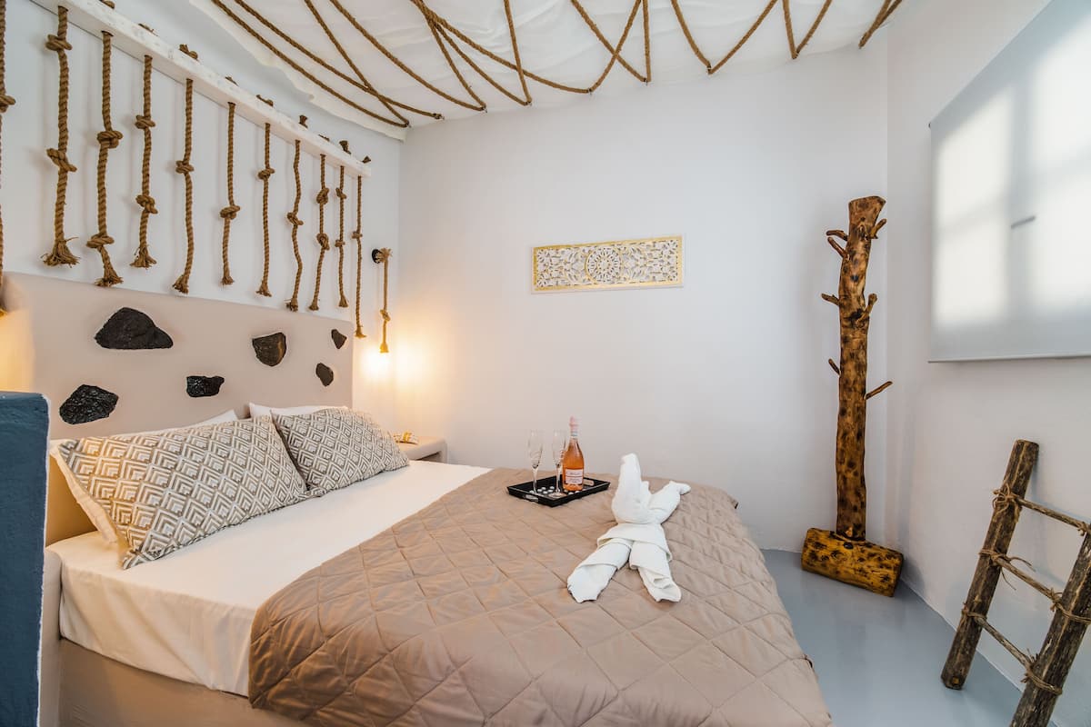 A neatly made bed with a patterned pillow, a tray with glasses and a bottle, and a towel on the bed.