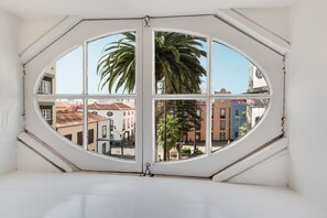 Une pièce dotée d’une grande fenêtre octogonale qui offre une vue sur les bâtiments et les palmiers.