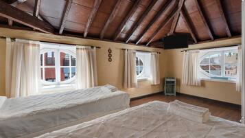 Una habitación con dos camas, vigas de madera en el techo, ventanas con cortinas y un televisor de pantalla plana.
