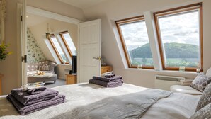 A bedroom with a large bed, two windows with a view, a door, and a small table with a plant. - Serendipity- Romantic 1-bed Apt Ambleside (Ambleside)