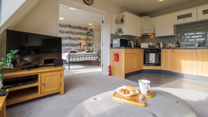 A modern kitchen with wooden cabinets, a microwave, and a dining area with a table and chairs. - Serendipity- Romantic 1-bed Apt Ambleside (Ambleside)