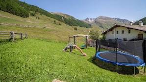 Una zona erbosa all'aperto con un'area giochi, un trampolino e una casa con tetto spiovente.