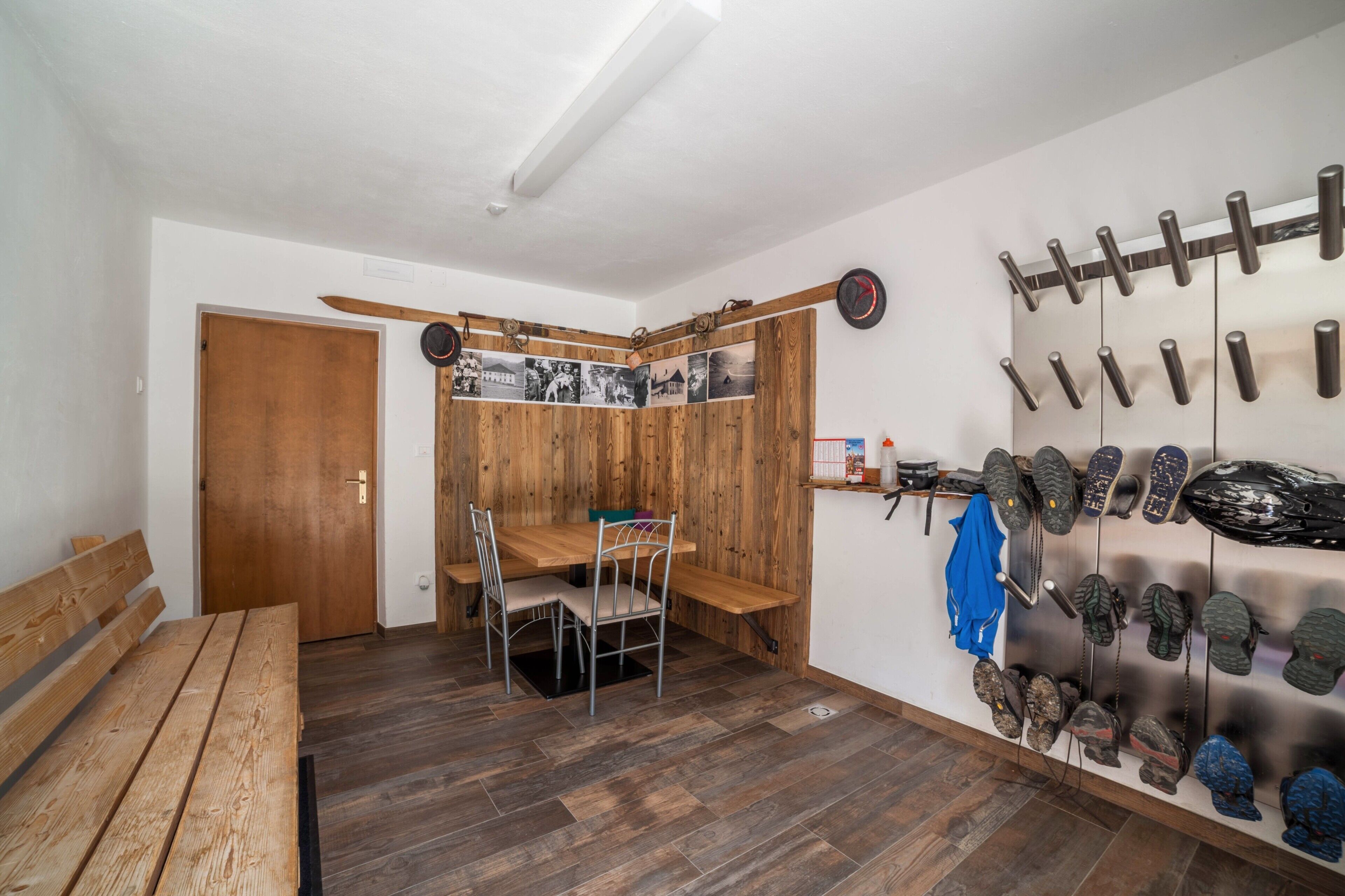 Une pièce comprenant un banc en bois, une table à manger avec des chaises, un porte-chaussures fixé au mur et une porte avec un panneau en bois.