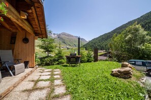 A wooden cabin with a stone fireplace, a gravel path, and a view of a mountain. - Apartment “Haus Fliri” in Etschtal Valley with Wi-Fi, Garden & Terrace (Graun im Vinschgau)