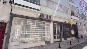 A multi-story building with a ground-floor shop, large windows, and a visible air conditioning unit. - Estudio T34 - City Historic Center (Lisboa)