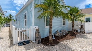A light blue house with a white picket fence, palm trees, and a dock.