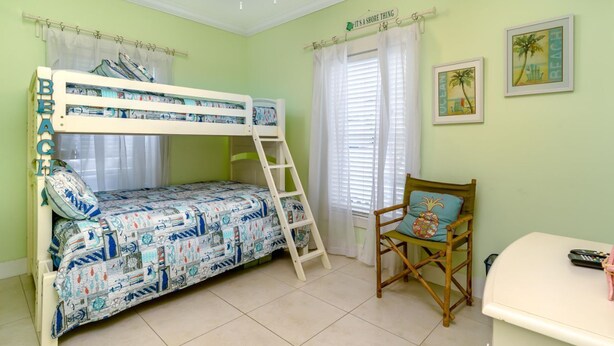 A bunk bed with a ladder, a chair with a pineapple cushion, a desk with a remote control, and two framed pictures on the wall.