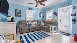 A living room with a sectional sofa, a ceiling fan, a television, and nautical-themed decorations.