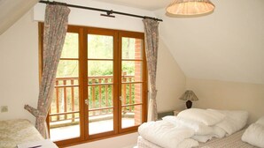 A bedroom with a large window, a bed, a bedside table with a lamp, and a chair.