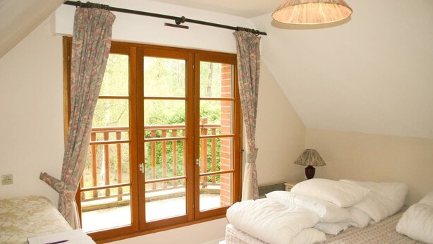 A bedroom with a large window, a bed, a bedside table with a lamp, and a chair.