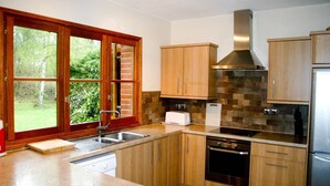 A modern kitchen with wooden cabinets, a stainless steel range hood, a dishwasher, and a large window with a view of greenery.