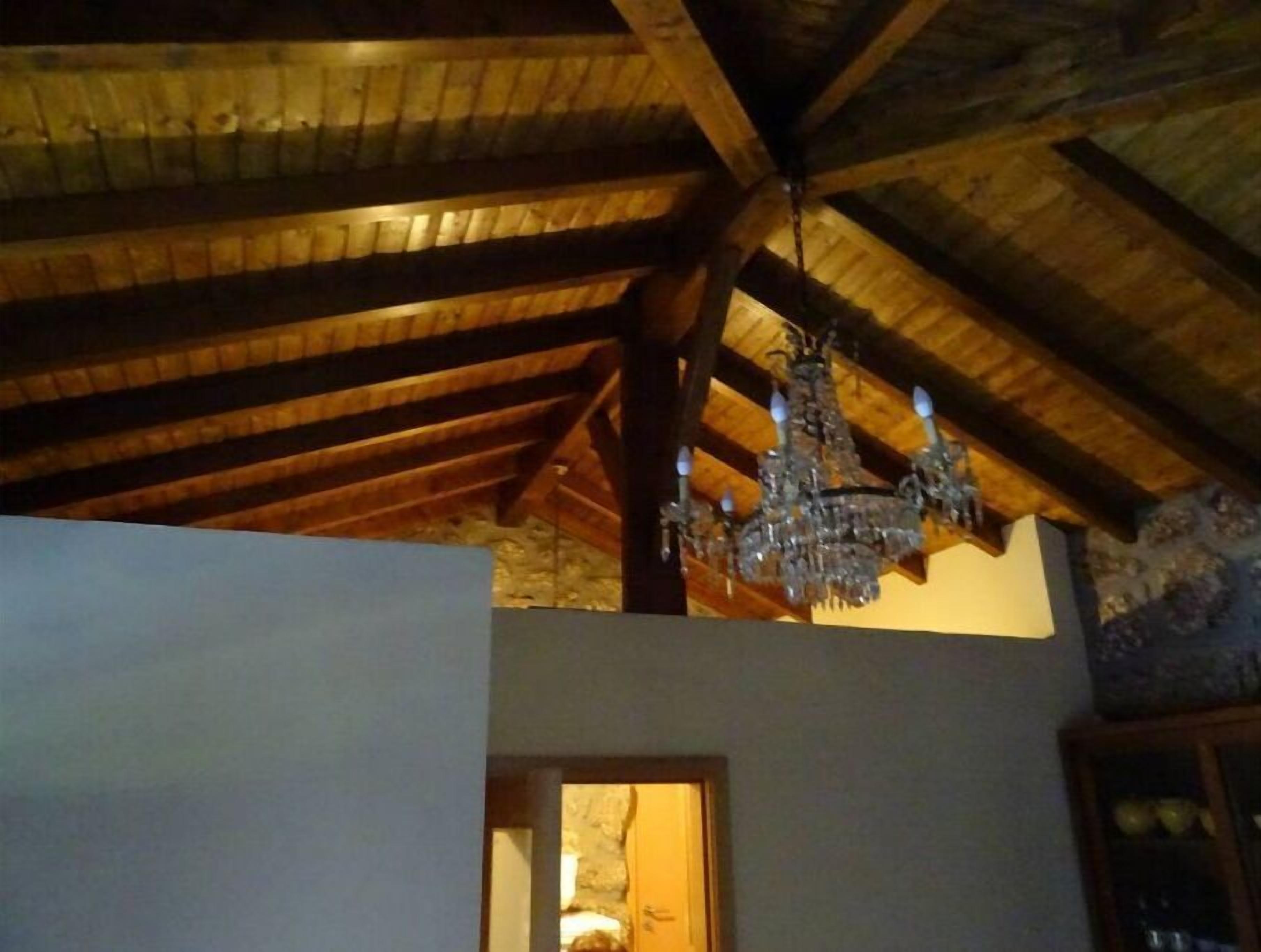 A room with exposed wooden beams, a chandelier, and a stone wall.