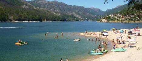 A beach with boats lined up, people swimming, and a mountainous backdrop.