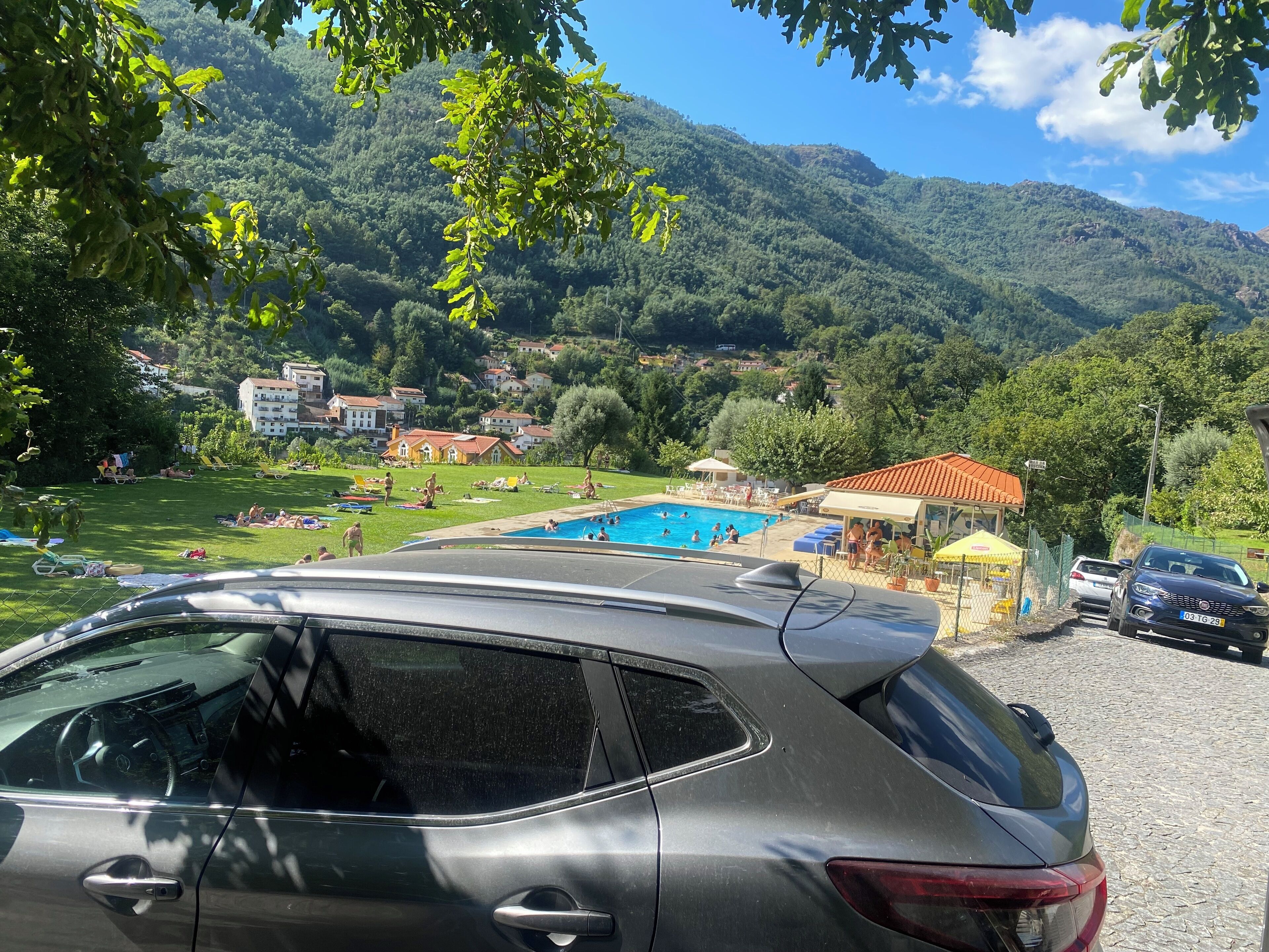 A swimming pool area with a view of a mountain range, surrounded by greenery and buildings.