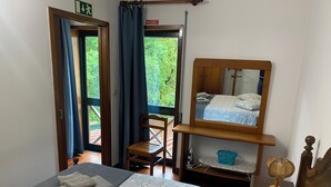 Une chambre à coucher avec un lit, une chaise, un miroir et une petite table sur laquelle se trouve un ventilateur.