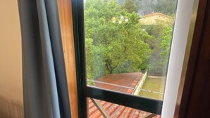 Une pièce dotée d’une grande fenêtre donnant sur une cour intérieure, avec un toit recouvert de tuiles et une végétation luxuriante.