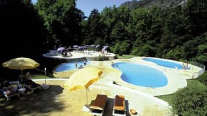 Une grande piscine extérieure divisée en plusieurs zones, entourée d’une végétation luxuriante et avec une chaîne de montagnes en toile de fond.