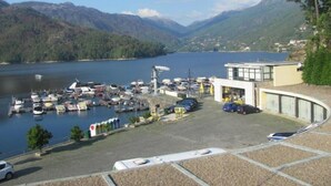 Un port de plaisance avec des bateaux amarrés, un espace de stationnement et un bâtiment doté de grandes fenêtres donnant sur un lac et des montagnes.