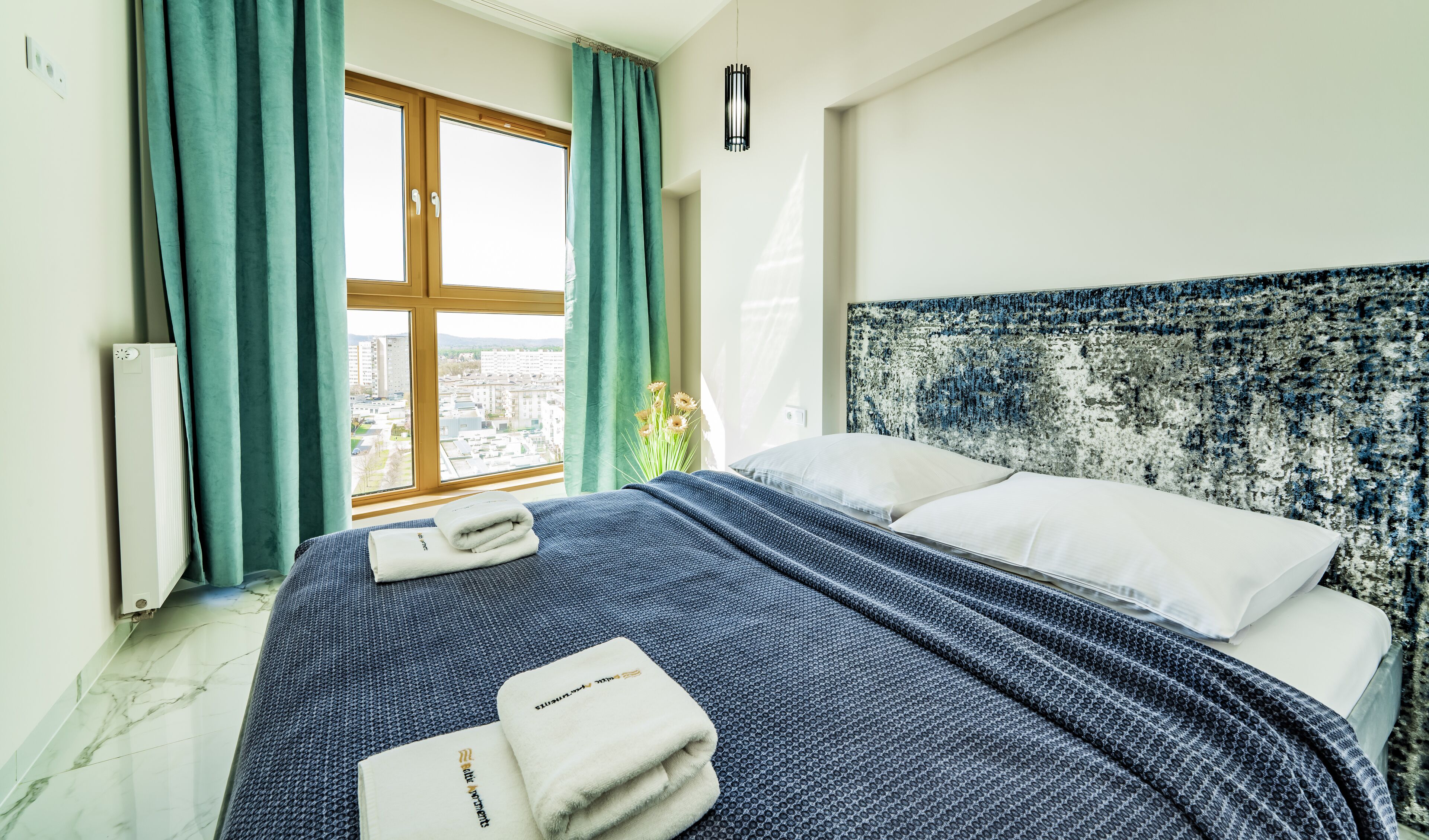 Ett hotellrum med en stor säng, utsikt över staden genom ett fönster och ett element på väggen.