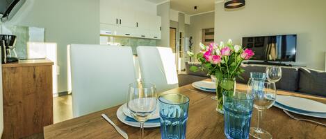 A dining area with a wooden table set for four, a vase with flowers, and a television in the background.