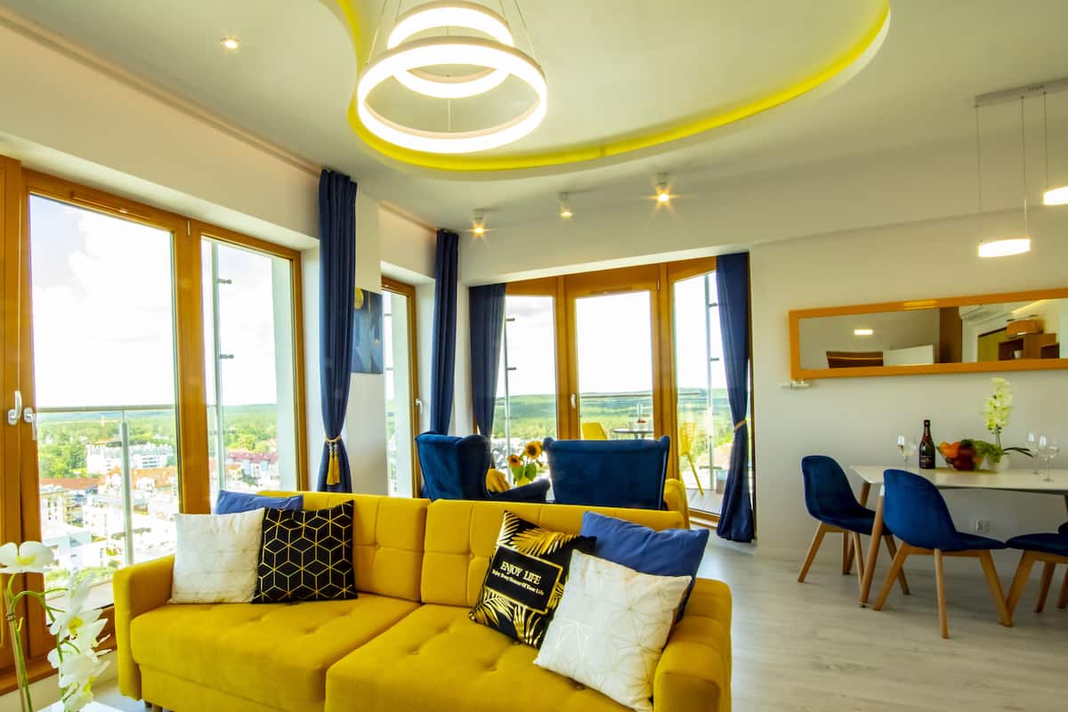 Un salon moderne avec un canapé jaune, des fauteuils bleus et un coin repas.