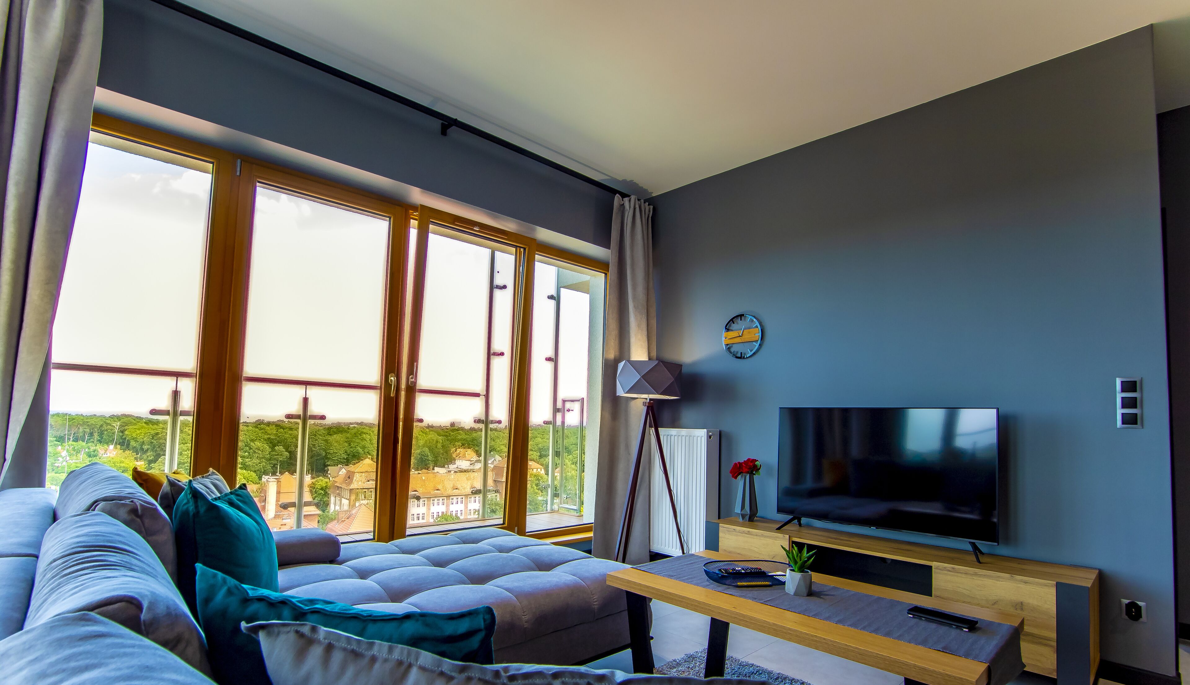 Un salon moderne avec une grande fenêtre, un canapé, un téléviseur et une lampe.