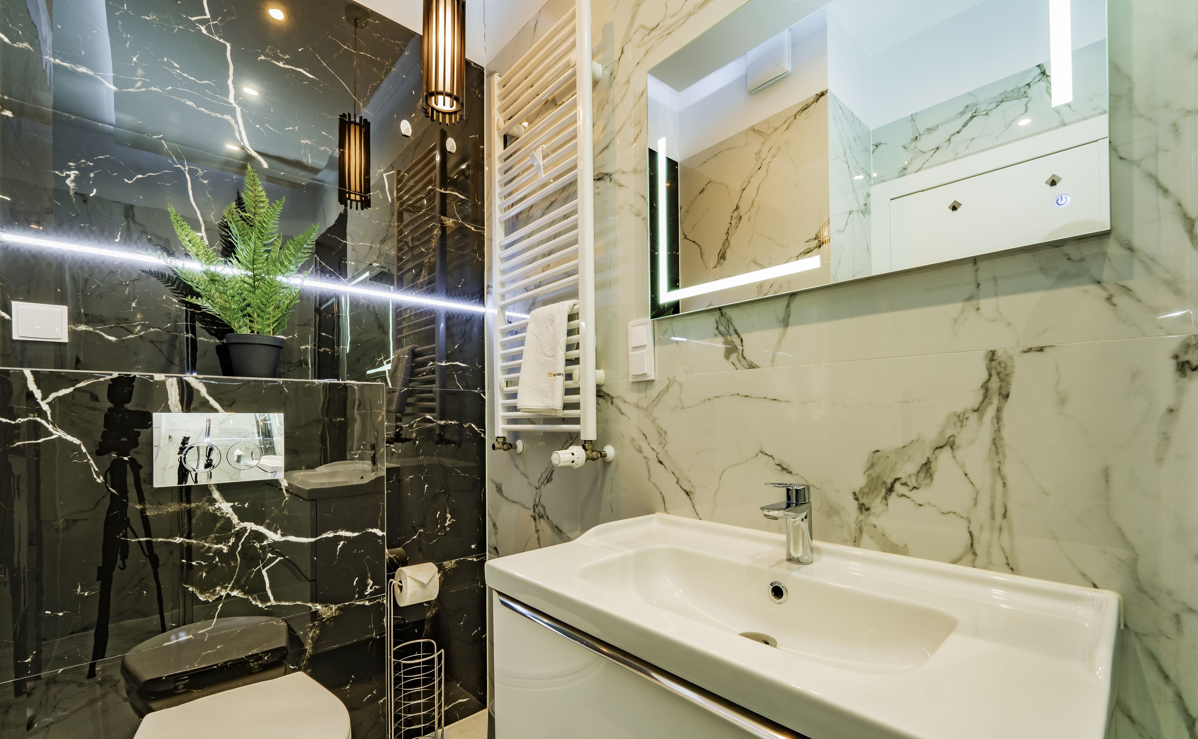 A modern bathroom with a white sink, black marble walls, and a mirror above the sink.