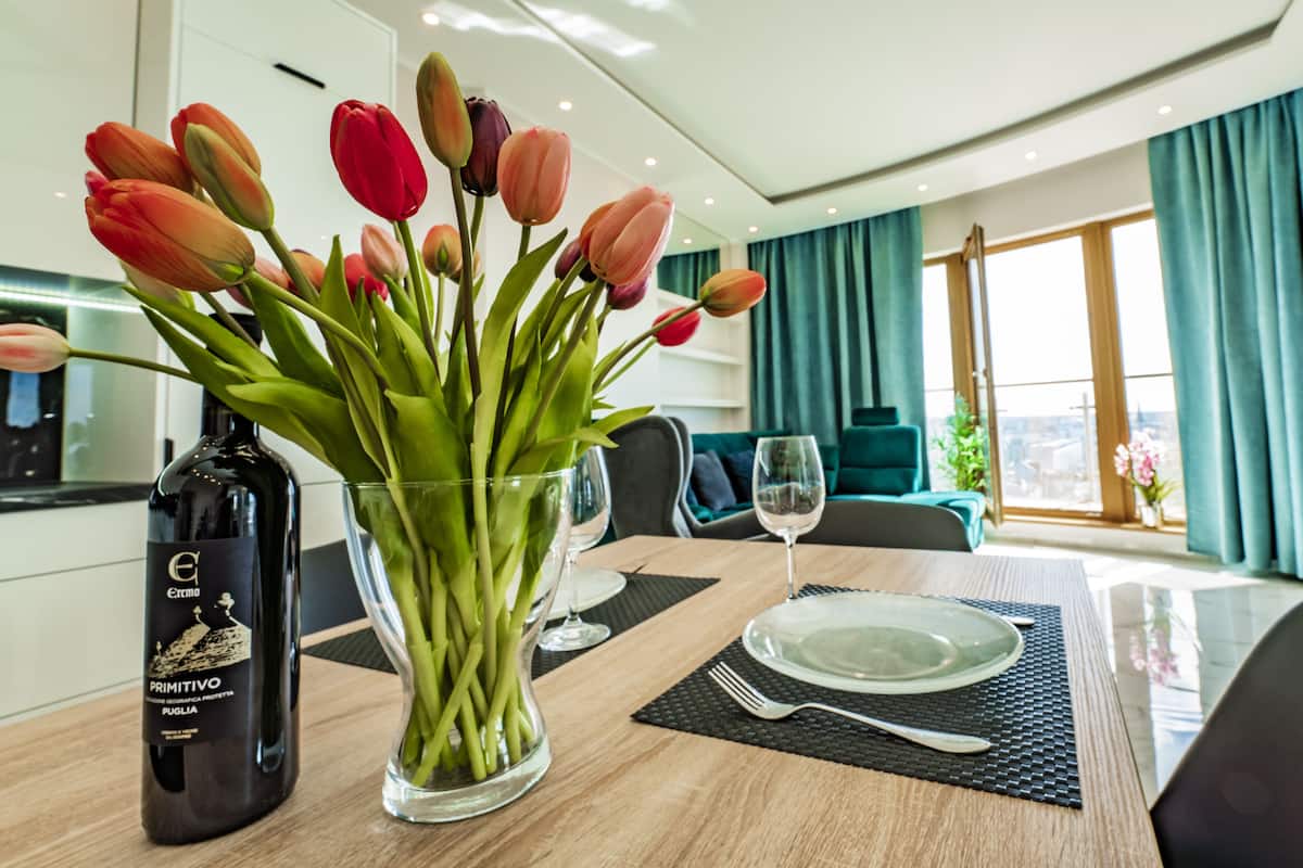 Une table à manger dressée avec une bouteille de vin, un vase de tulipes et un verre d’eau.