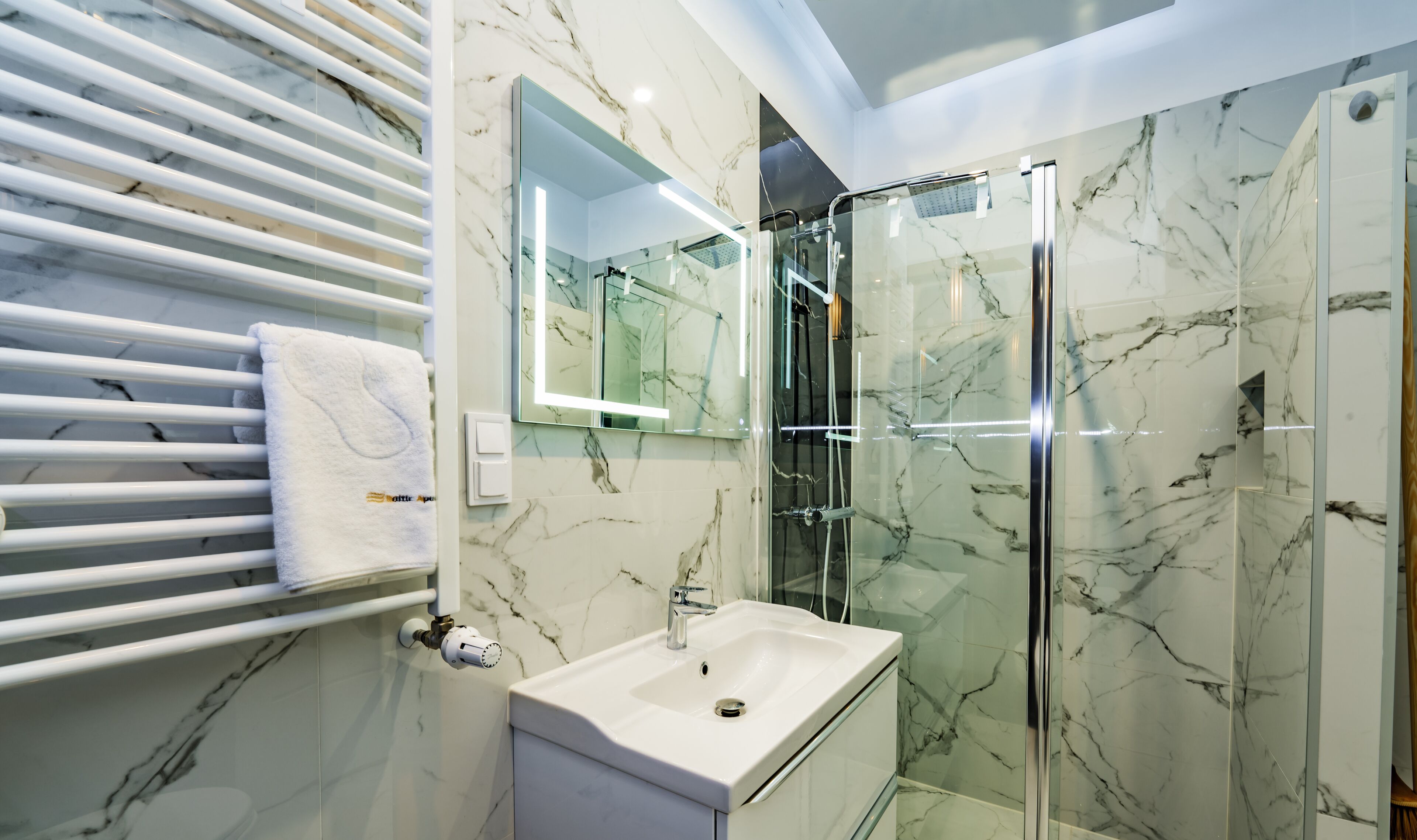 Ein modernes Badezimmer mit Glasdusche, Waschbecken in Weiß und einem Handtuchhalter.