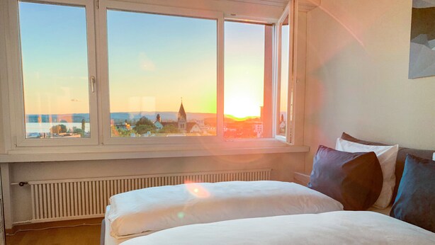 A bedroom with a large window, a bed, and a radiator. - Lake View Business Apartment (Zug)
