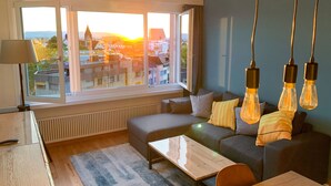 A modern living room with a sofa, coffee table, and a view of a cityscape through large windows. - Lake View Business Apartment (Zug)