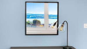 A room with a desk, a yellow chair, a framed picture of a landscape, and two hanging light bulbs. - Lake View Business Apartment (Zug)