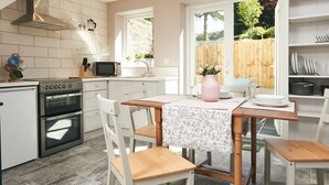 A kitchen with white cabinets, a built-in oven, a microwave, and a dining area with a table and chairs. - Perfect romantic break-  cottage in Laugharne (Laugharne)