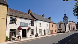 A street with a white building with a clock tower, a signboard, and flower baskets. - Perfect romantic break-  cottage in Laugharne (Laugharne)