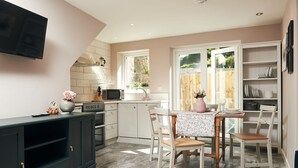 A modern kitchen with a dining area, featuring a TV, microwave, and a large window. - Perfect romantic break-  cottage in Laugharne (Laugharne)