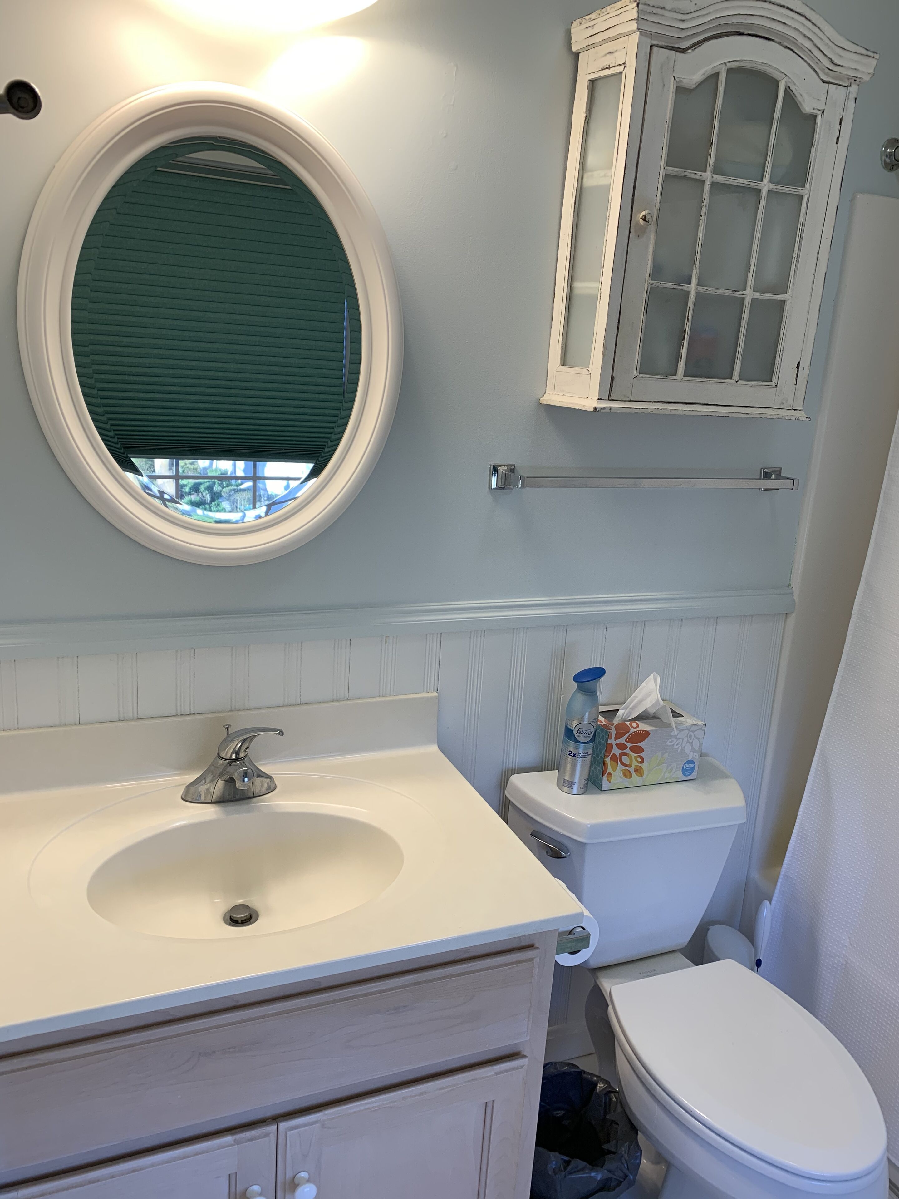 Une salle de bain avec un lavabo blanc, un miroir rond, des toilettes et un meuble de rangement.
