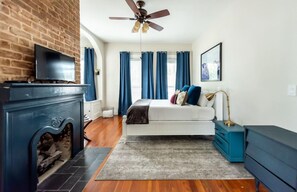 A modern bedroom with a fireplace, a bed, a TV, and a ceiling fan. - Designer Victorian Apartment Close to Forsyth, Nightlife by Lucky Savannah (Savannah)