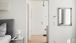 Habitación de hotel con cama, mesita de noche con lámpara, espejo y puerta que da a otra habitación.