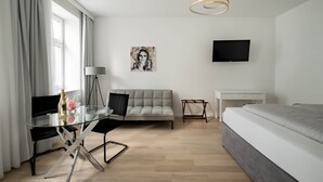 Una habitación de hotel moderna con una mesa de comedor de vidrio, un sofá, una cama, un televisor y un cuadro en la pared.