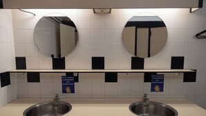 Een toiletruimte met twee wastafels, twee spiegels en een plank boven de wastafels.