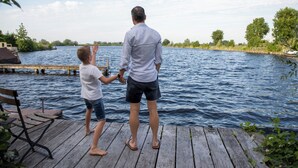 Een houten steiger die uitstulpt over het water, met een persoon en een kind erop.