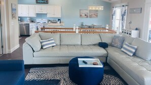A modern living room with a sectional sofa, a dining area, and a kitchen. - 218 Brunswick in Holden Beach, perfect for family getaways! (Holden Beach)