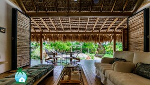 A spacious room with a wooden floor, a sofa, a dining table, and a thatched roof.