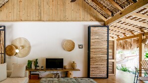 A cozy living room with a wooden ceiling, a flat-screen TV, a sofa, and a coffee table with books and candles.