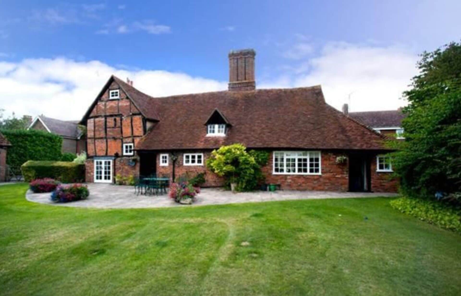 A traditional half-timbered house with a steeply pitched roof, a central chimney, and a well-maintained lawn in the foreground.