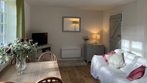 Ein gemütliches Wohnzimmer mit Holztisch, weißem Sofa, Fernseher und Blumenvase.