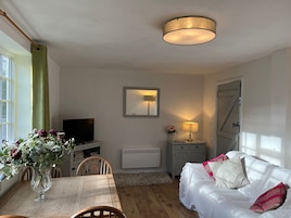 Una sala de estar acogedora con una mesa de madera, un sofá blanco, un televisor y un jarrón de flores.