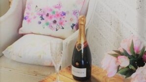 Ein Holztisch mit einer Champagnerflasche, einem Glas und einer Blumenkomposition.