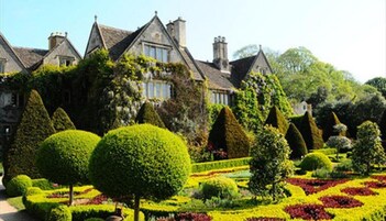 Un edificio histórico con un jardín formal, con setos recortados y macizos de flores.